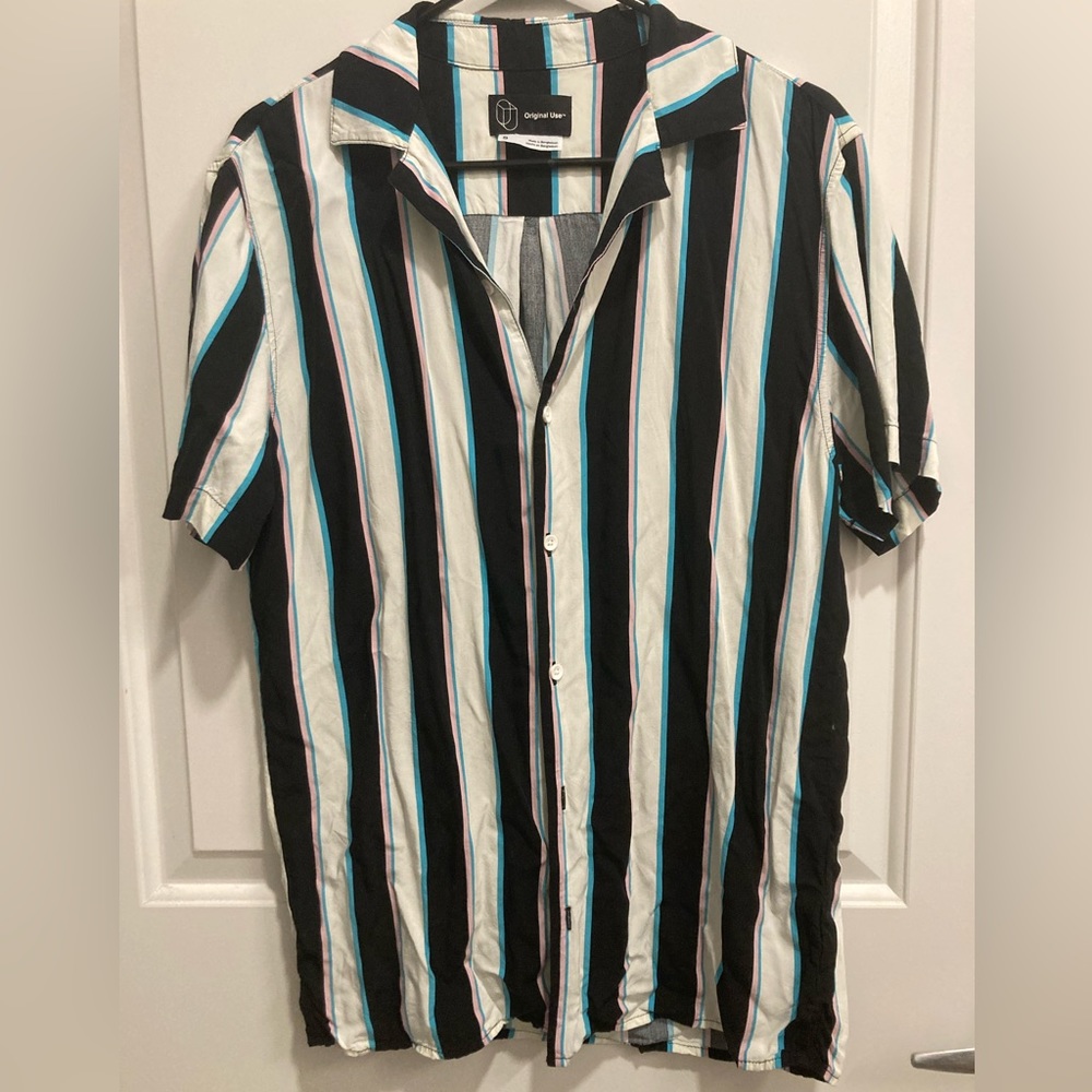 Men’s short sleeve button up with black/white/blue/pink vertical stripe pattern.
